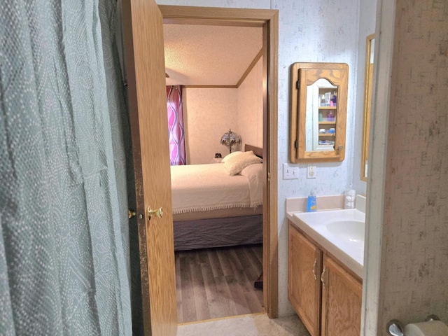 full bath with a textured ceiling, wood finished floors, vanity, ensuite bath, and wallpapered walls