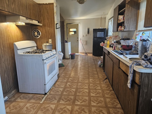 kitchen featuring under cabinet range hood, white range with gas cooktop, light countertops, freestanding refrigerator, and open shelves