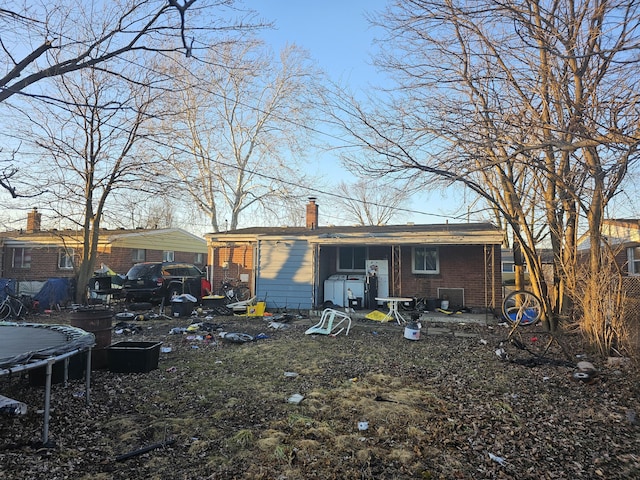 rear view of house with a trampoline, brick siding, and a chimney