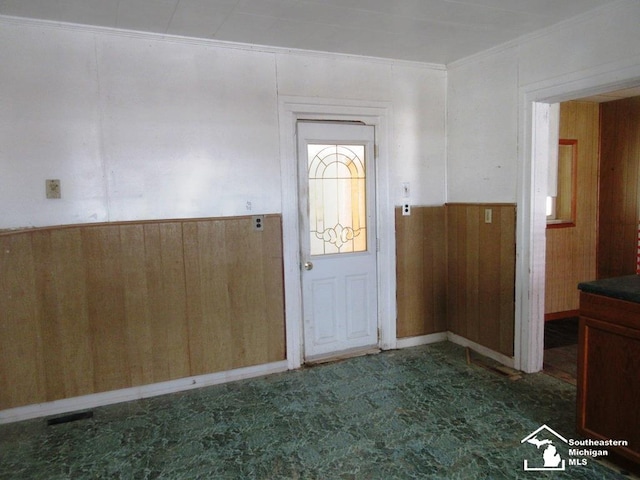 entryway featuring a wainscoted wall, crown molding, and wooden walls