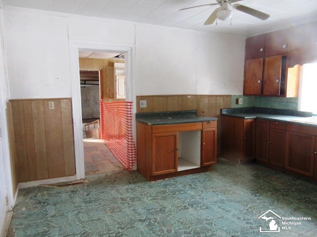 kitchen with a wainscoted wall, brown cabinets, a ceiling fan, and wooden walls