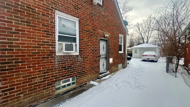 view of snow covered exterior featuring a detached garage, an outdoor structure, and brick siding