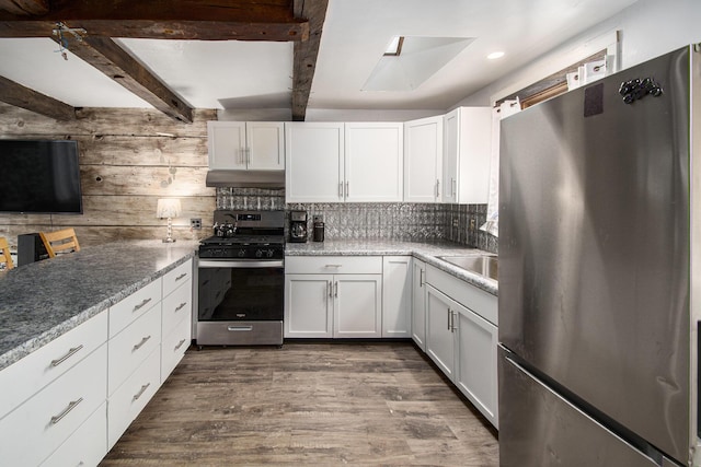 kitchen featuring white cabinets, appliances with stainless steel finishes, dark wood-style flooring, under cabinet range hood, and beam ceiling