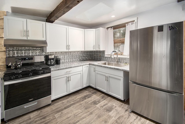 kitchen with light wood finished floors, tasteful backsplash, appliances with stainless steel finishes, under cabinet range hood, and a sink