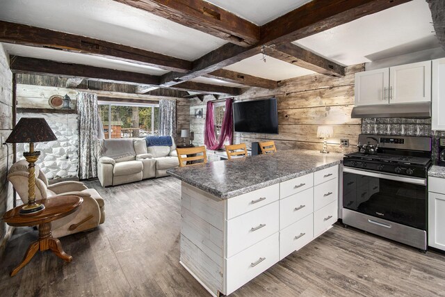 kitchen featuring under cabinet range hood, a peninsula, wood finished floors, stainless steel range with gas cooktop, and beam ceiling