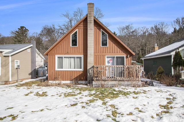 snow covered rear of property featuring board and batten siding and a chimney