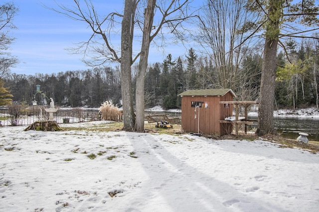 snowy yard featuring a shed, fence, and an outbuilding