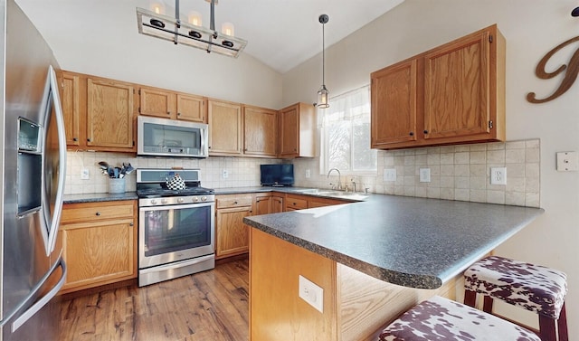 kitchen with wood finished floors, a peninsula, vaulted ceiling, stainless steel appliances, and a sink