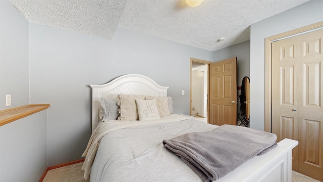 bedroom featuring a closet, light colored carpet, a textured ceiling, and baseboards