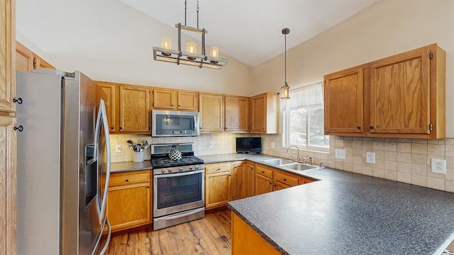 kitchen featuring dark countertops, decorative light fixtures, a peninsula, stainless steel appliances, and a sink