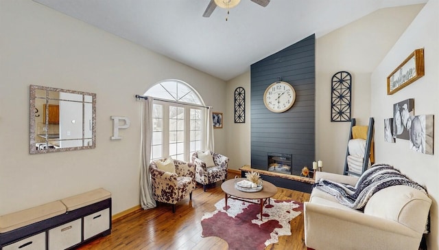 living room with lofted ceiling, ceiling fan, hardwood / wood-style flooring, a large fireplace, and baseboards