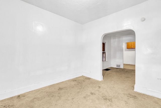 spare room featuring carpet floors, arched walkways, visible vents, and baseboards