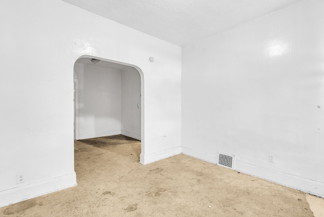 carpeted empty room with visible vents, arched walkways, and baseboards