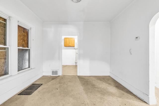 carpeted empty room featuring baseboards, visible vents, and arched walkways