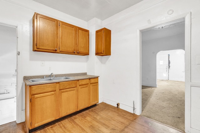 kitchen featuring arched walkways, light carpet, a sink, light wood-type flooring, and brown cabinets