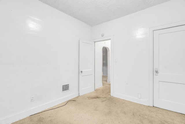 unfurnished bedroom with visible vents, arched walkways, baseboards, carpet, and a textured ceiling