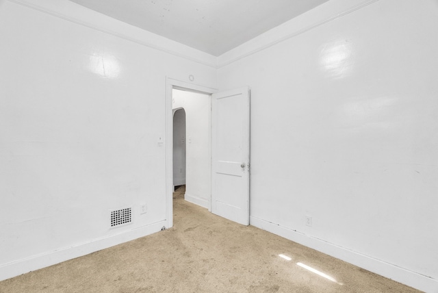 empty room with carpet floors, arched walkways, visible vents, ornamental molding, and baseboards