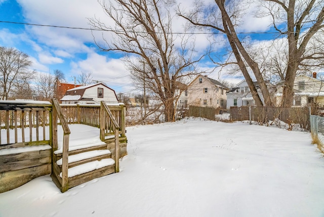 yard covered in snow featuring a wooden deck, fence, and a residential view