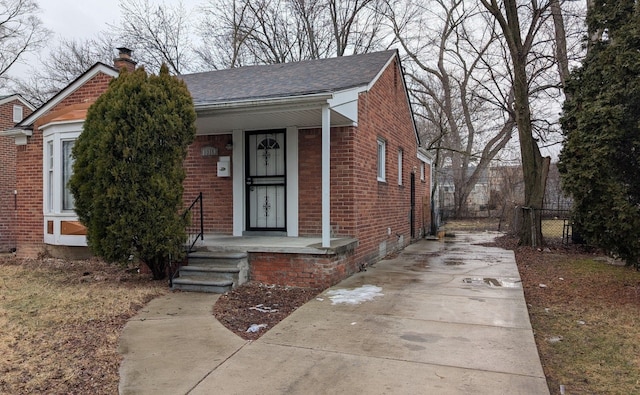 bungalow featuring a shingled roof, a chimney, covered porch, fence, and brick siding