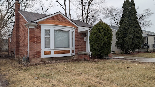 bungalow-style house with a front yard, brick siding, a chimney, and roof with shingles