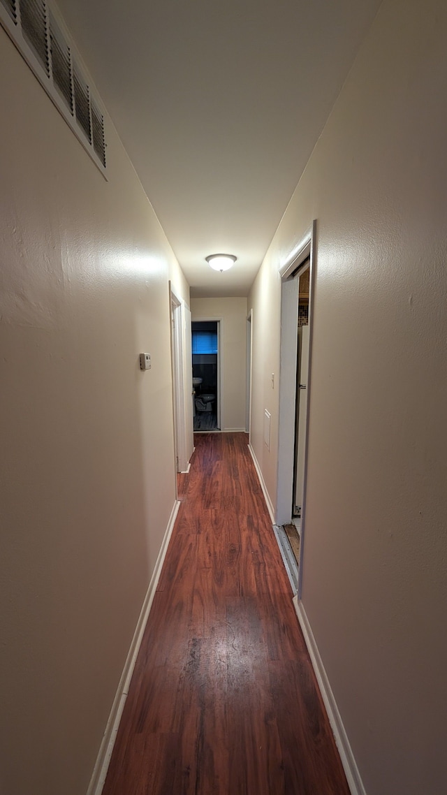 hall featuring wood finished floors, visible vents, and baseboards