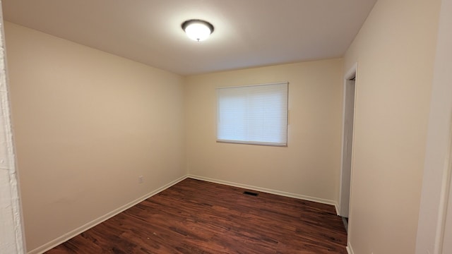 empty room featuring visible vents, dark wood finished floors, and baseboards