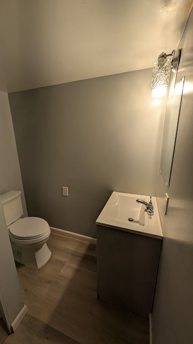 half bath with baseboards, vanity, toilet, and wood finished floors