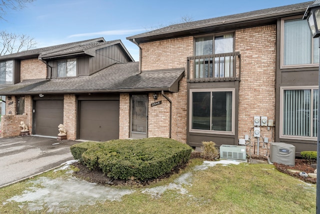 multi unit property featuring driveway, a shingled roof, cooling unit, and brick siding