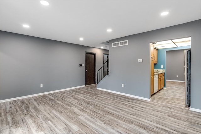 unfurnished room with visible vents, light wood-style flooring, baseboards, and stairs