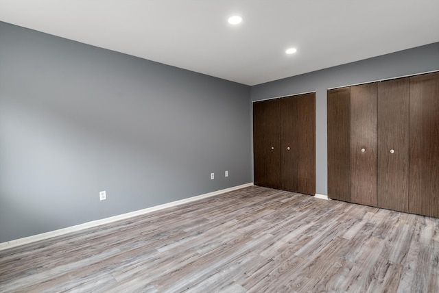 unfurnished bedroom with recessed lighting, light wood-style flooring, baseboards, and two closets