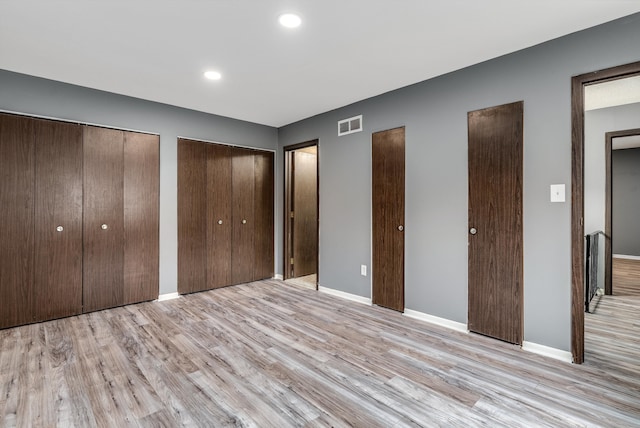 unfurnished bedroom featuring baseboards, visible vents, light wood-type flooring, two closets, and recessed lighting