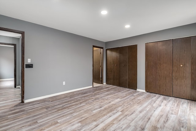 unfurnished bedroom featuring light wood finished floors, multiple closets, recessed lighting, and baseboards