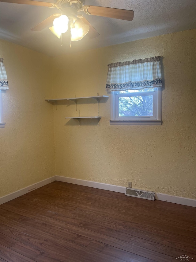 interior space featuring a ceiling fan, visible vents, dark wood finished floors, and baseboards