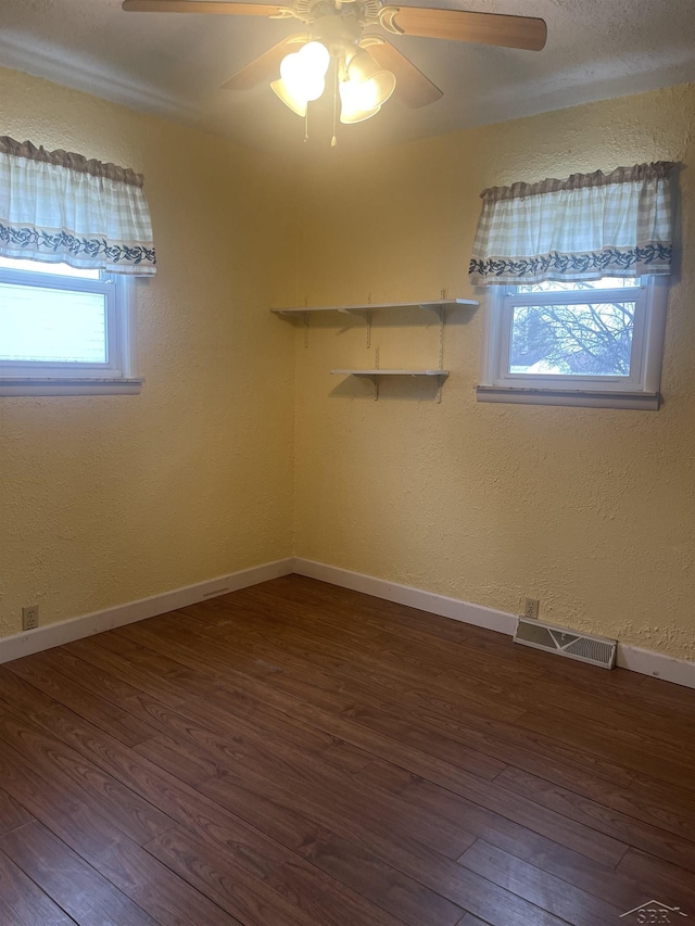 unfurnished room featuring dark wood-style floors, a ceiling fan, visible vents, and baseboards