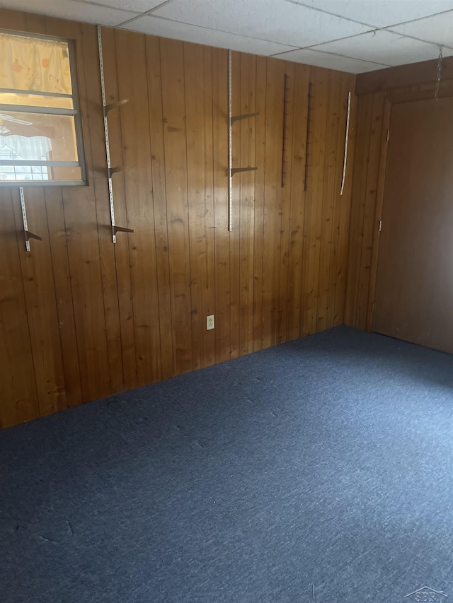 carpeted empty room featuring a paneled ceiling and wood walls