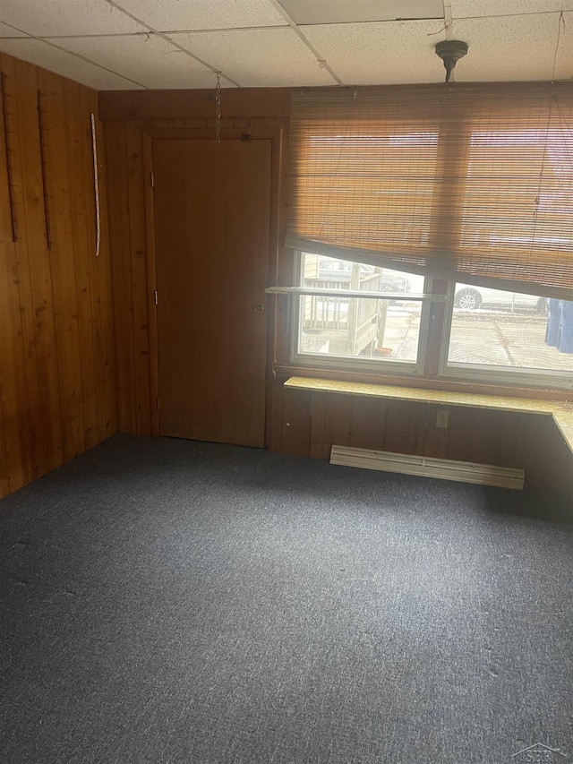 carpeted empty room featuring a paneled ceiling and wood walls