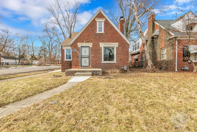 view of front of home featuring a front yard, brick siding, and a chimney