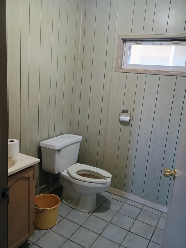 half bathroom with toilet, wood walls, vanity, and tile patterned floors