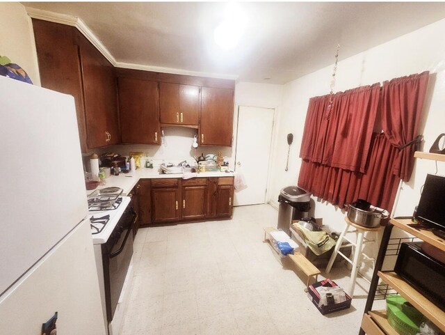 kitchen with range with gas cooktop, light floors, light countertops, freestanding refrigerator, and a sink