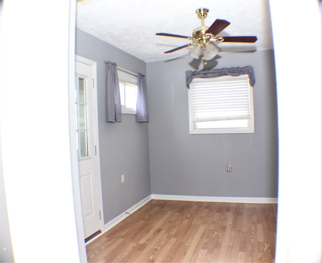 unfurnished room with light wood-style floors, a textured ceiling, baseboards, and a ceiling fan