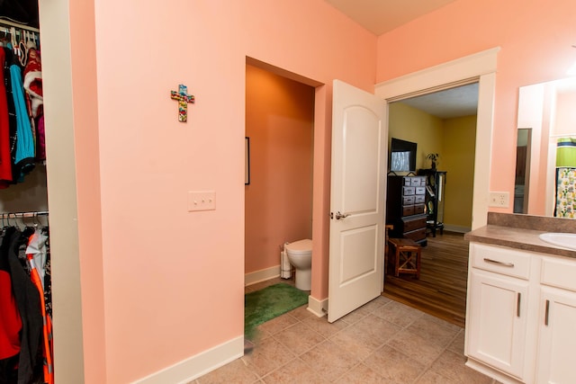 full bath with toilet, baseboards, a walk in closet, and vanity