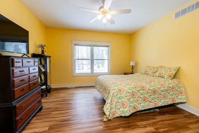 bedroom with ceiling fan, wood finished floors, visible vents, and baseboards