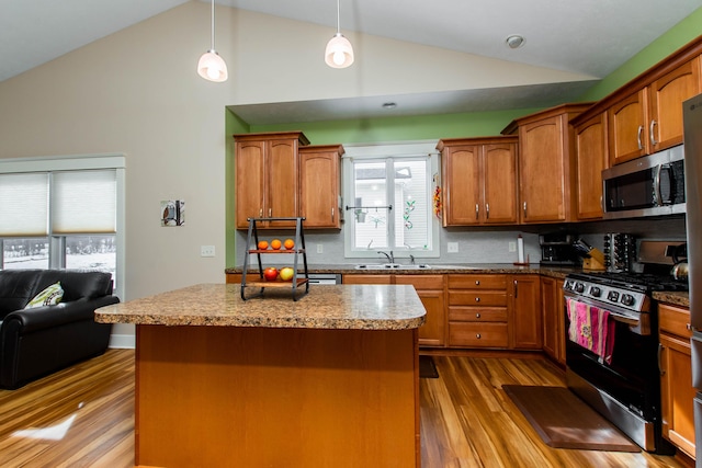 kitchen featuring pendant lighting, brown cabinets, stainless steel appliances, an island with sink, and wood finished floors