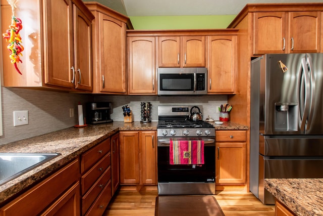 kitchen with stainless steel appliances, light wood-style flooring, decorative backsplash, and light stone countertops