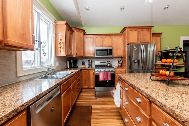 kitchen featuring stainless steel appliances, a sink, backsplash, brown cabinets, and light wood finished floors