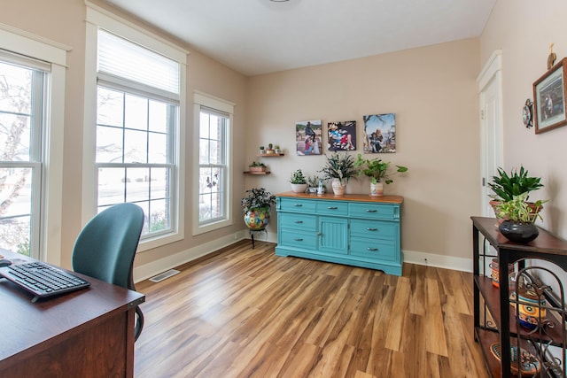 office space with light wood-type flooring, visible vents, and baseboards