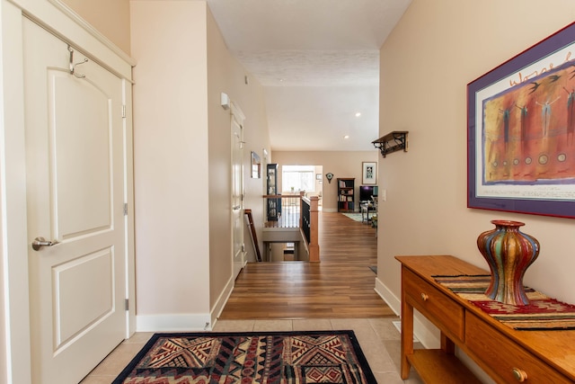 hall featuring light tile patterned floors, an upstairs landing, and baseboards