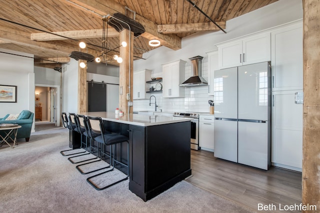 kitchen featuring a barn door, wooden ceiling, wall chimney range hood, stainless steel electric range, and freestanding refrigerator