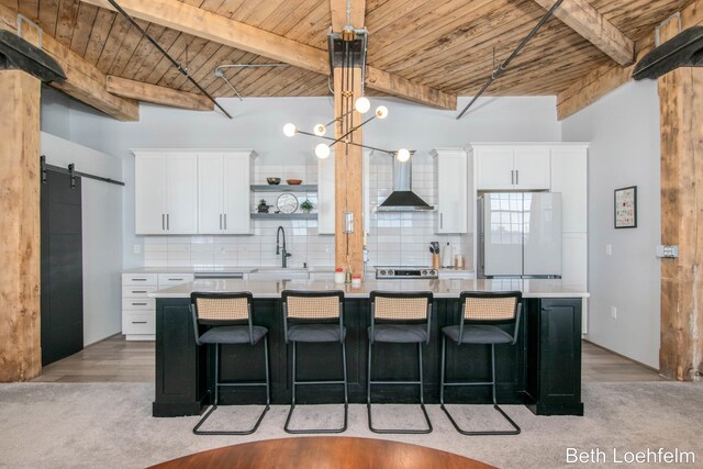 kitchen with wall chimney exhaust hood, a barn door, wooden ceiling, and freestanding refrigerator