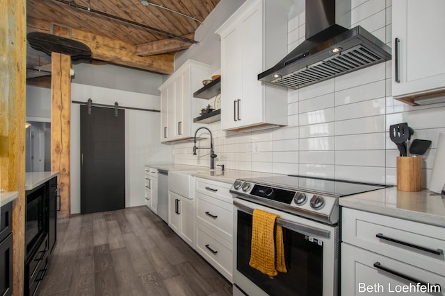 kitchen featuring a barn door, open shelves, a sink, appliances with stainless steel finishes, and wall chimney exhaust hood